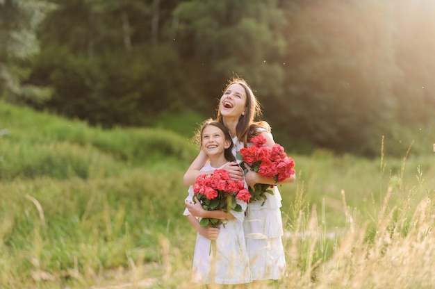 Dos hermanas vestidas con vestidos blancos se divierten juntas en verano. Las niñas sostienen flores.