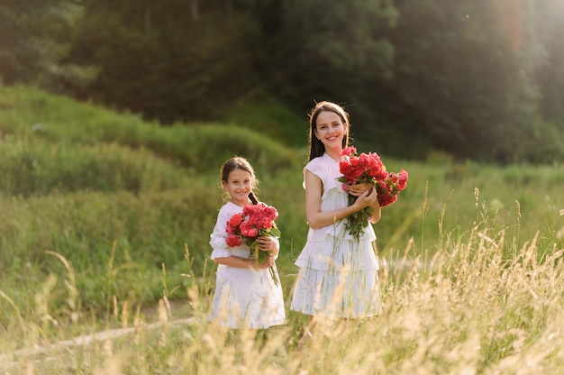 Dos hermanas vestidas con vestidos blancos se divierten juntas en verano. Las niñas sostienen flores.