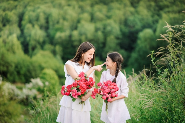Dos hermanas vestidas con vestidos blancos se divierten juntas en verano. Las niñas sostienen flores.