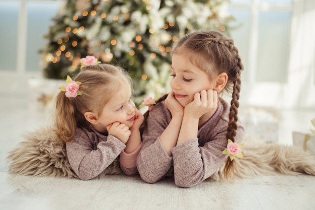 Dos hermanas yacen bajo el árbol de navidad.