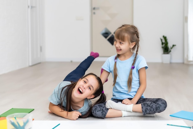 dos hermanitas se acuestan en el suelo de la casa y dibujan con lápices de colores sobre papel. los niños hacen tareas creativas después de la escuela.