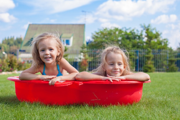 Dos hermanitas retozando y chapoteando en su patio en una pequeña piscina