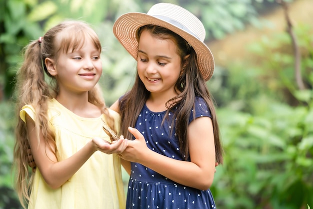 Dos hermanitas sosteniendo una mariposa en sus manos. Niños explorando la naturaleza. Ocio familiar con niños en verano.