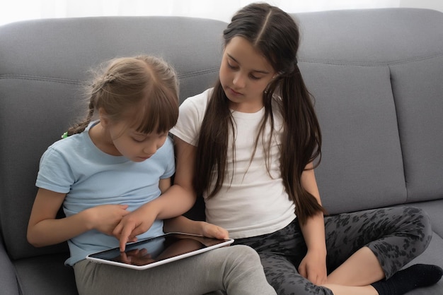 Dos hermanitas usando tableta en casa. Viendo algo divertido.