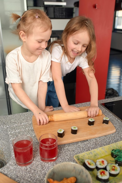 Dos hermanitos divirtiéndose y comiendo en la cocina de casa con comida japonesa