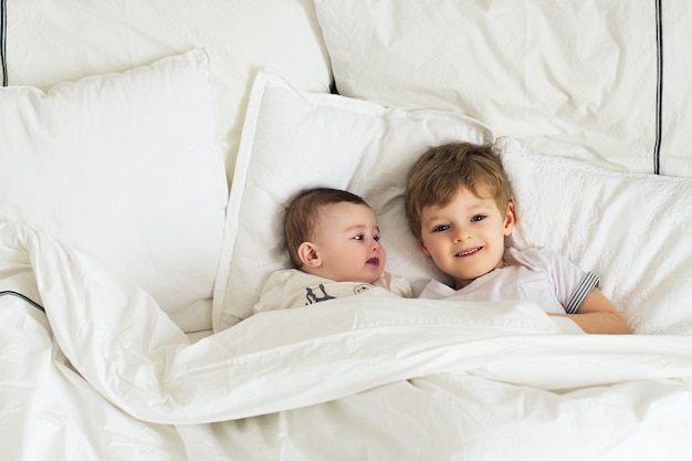 Dos hermanitos muy sonrientes en la cama, mañana divertida