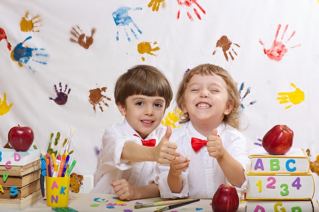 Dos hermanos de 7 y 4 años vestidos con camisetas blancas con lazos rojos están jugando juntos.