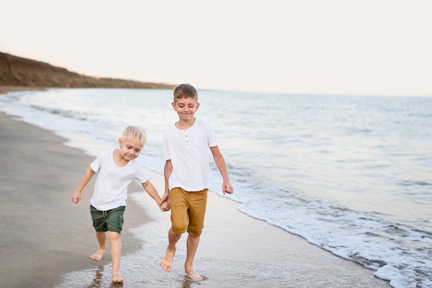 Dos hermanos caminan de la mano por la costa del mar. Vacaciones familiares. Amistad