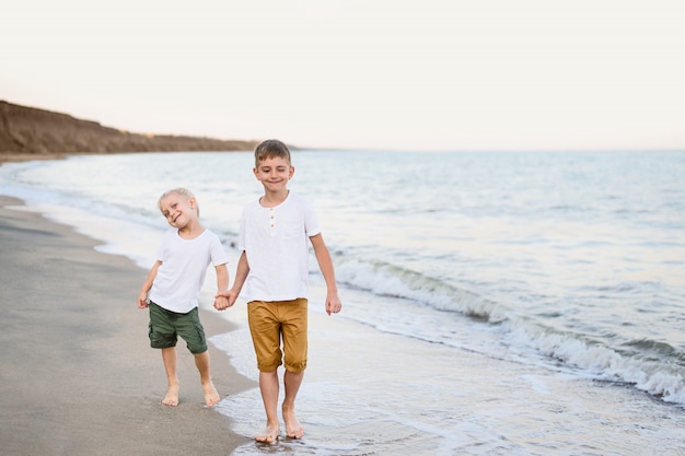 Dos hermanos caminan de la mano por la costa del mar.