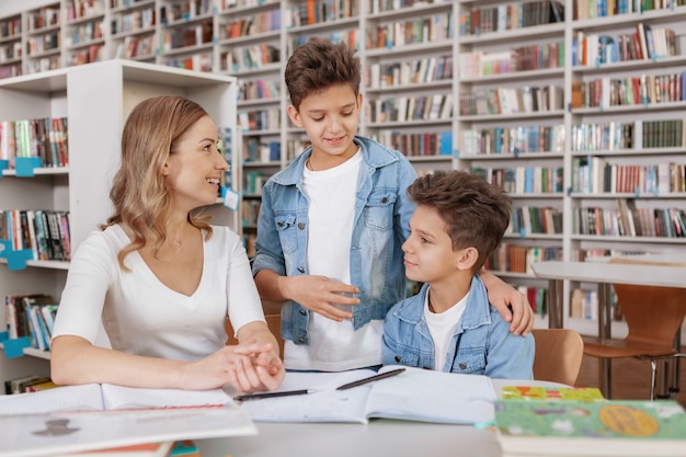 Dos hermanos gemelos y su madre disfrutando de estudiar juntos en la biblioteca.