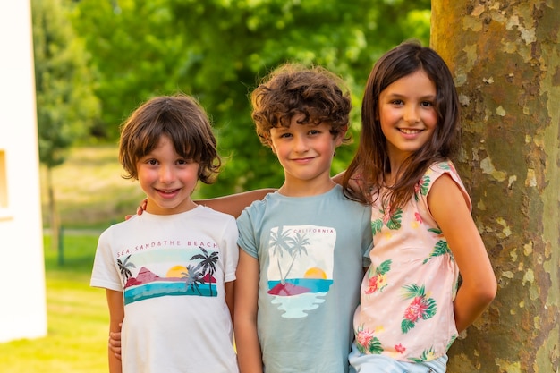 Dos hermanos y una hermana sonriendo en un parque junto a un árbol