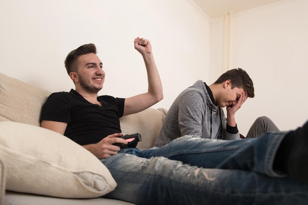 Dos hermanos o amigos jugando videojuegos juntos mientras se relajan en un sofá en la sala de estar