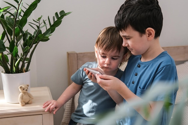 Dos hermanos pequeños felizmente viendo dibujos animados juntos en un teléfono inteligente Concepto de niños y gadgets