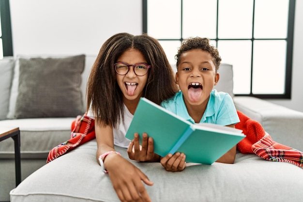 Dos hermanos tirados en el sofá leyendo un libro sacando la lengua felices con una expresión graciosa. concepto de emoción.