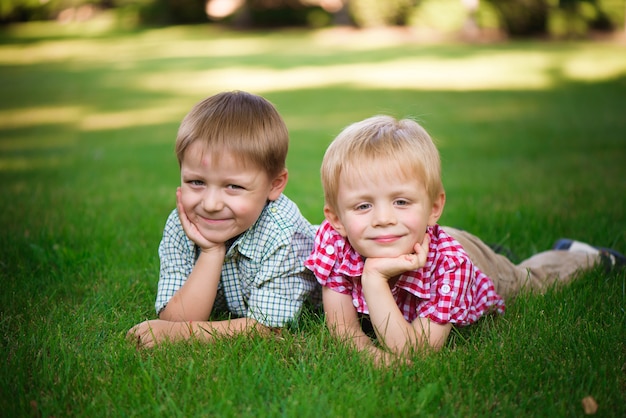 Dos hermanos tumbados en la hierba en un parque al aire libre, sonriendo y