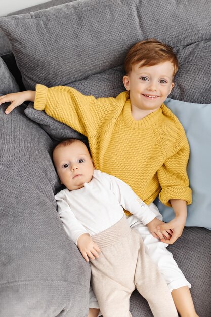 Dos hermanos yacen en un sofá gris en casa