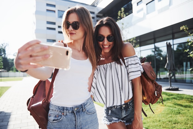 Dos hermosa joven estudiante feliz con mochila cerca del campus de la universidad y hacen una foto selfie. Concepto de educación y ocio