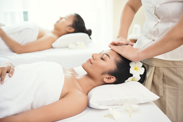 Dos hermosa mujer joven recibiendo salón de masaje spa y flor blanca en su oreja.