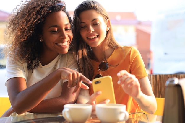 Dos hermosa mujer joven sentada en la cafetería tomando café y mirando el teléfono móvil.