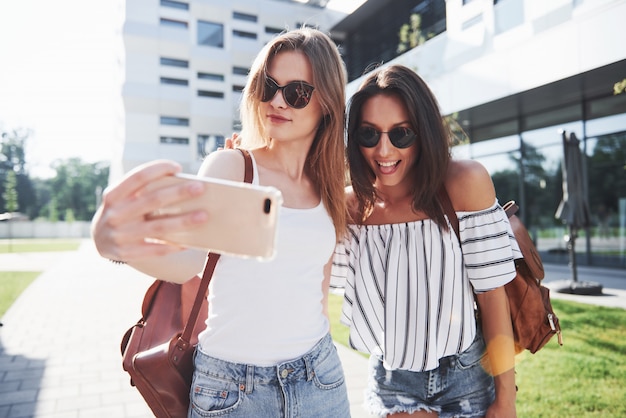 Dos hermosa niña feliz joven estudiante con mochila cerca del campus de la universidad y hacer foto selfie. Concepto de educación y ocio