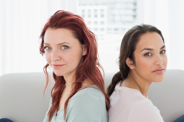 Dos hermosas amigas jóvenes sentados espalda contra espalda