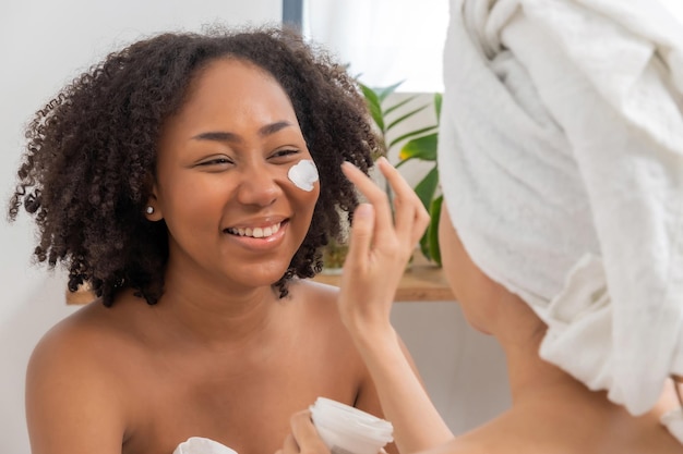 Foto dos hermosas amigas jóvenes en una toalla aplicando una máscara nutritiva blanca en la cara en la habitación de la cama en casa tratamiento facial cuidado de la piel tratamiento de belleza cosmético spa concepto de máscara facial corporal saludable