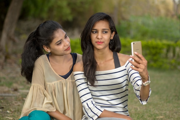 Dos hermosas amigas tomando selfie con smartphone al aire libre.