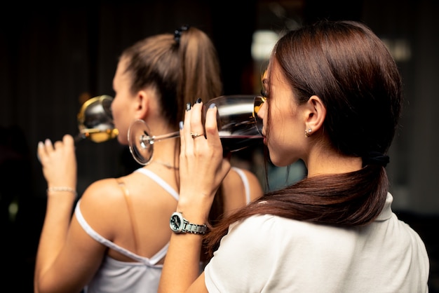 Dos hermosas chicas en blusas blancas beben vino de copas