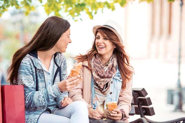 Dos hermosas chicas comiendo sándwiches y comprando