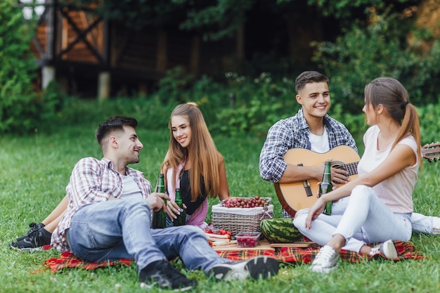 Dos hermosas chicas con dos chicos sentados en un parque sobre una manta con guitarra