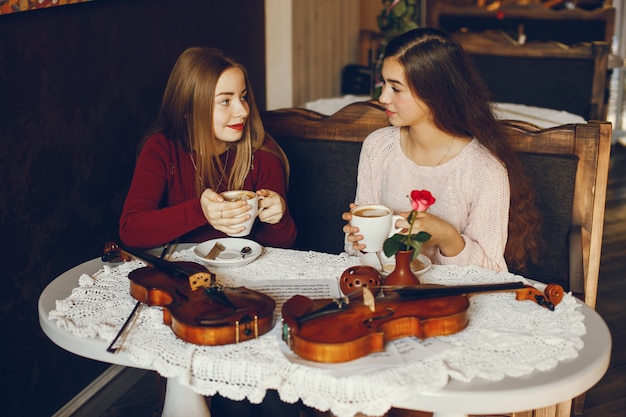 dos hermosas chicas elegantes sentados en un café con violín y tomando café