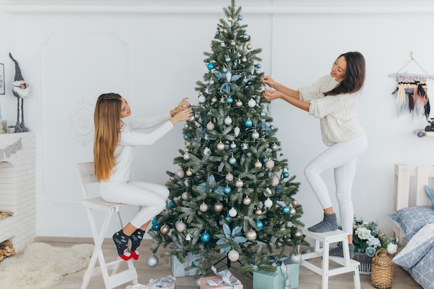 Dos hermosas chicas están decorando un árbol de Navidad.