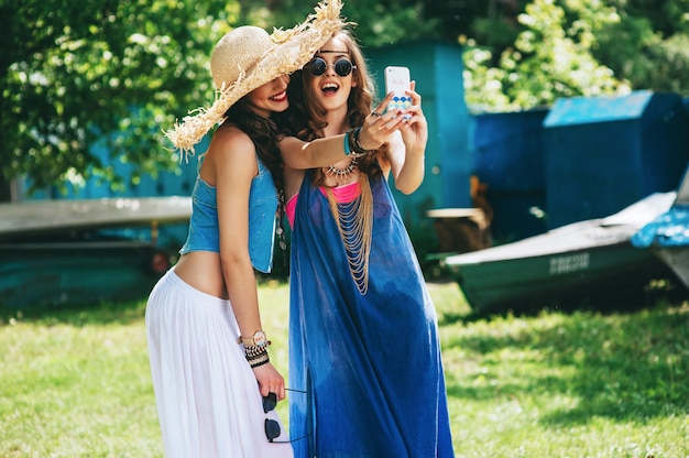 Dos hermosas chicas hippie para hacer selfie cerca de un barco viejo.