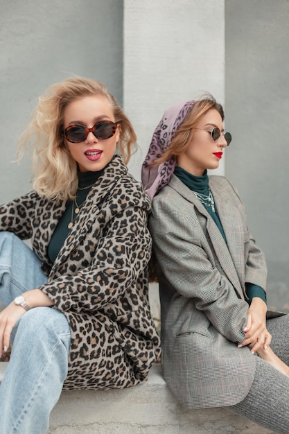 Dos hermosas chicas hipster de moda feliz con gafas de sol en ropa de moda se sienta en la calle