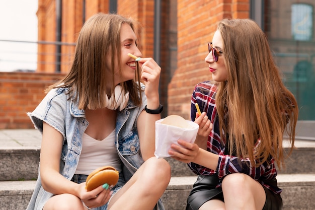 Dos hermosas chicas jóvenes comen comida rápida en la calle.