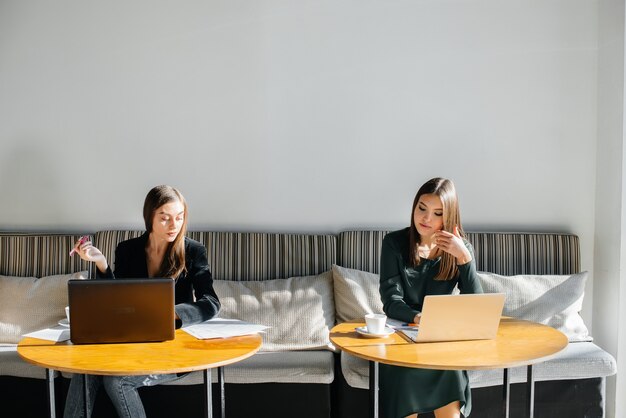 Dos hermosas chicas jóvenes están sentadas en un café, grabando blogs de video y comunicándose en las redes sociales.