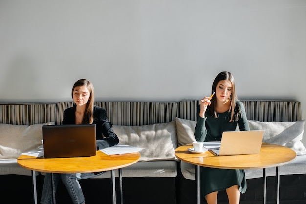 Dos hermosas chicas jóvenes están sentadas en un café, grabando blogs de video y comunicándose en las redes sociales.