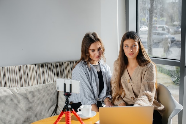 Dos hermosas chicas jóvenes están sentadas en un café, grabando blogs de video y comunicándose en las redes sociales.