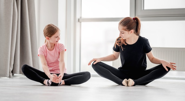 Dos hermosas chicas jóvenes haciendo piernas estiradas sentados en el suelo en posición de mariposa durante la clase de coreografía de danza ballet