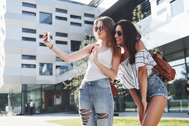 Dos hermosas chicas con mochilas caminan juntas en la ciudad. amigos muy lindos comparten secretos.