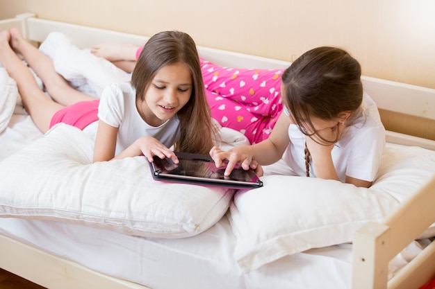 Dos hermosas chicas en pijama acostado en la cama y con tableta digital