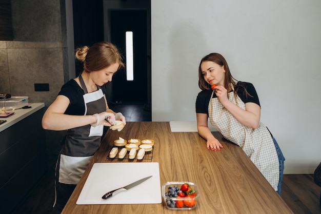 Dos hermosas chicas preparan pasteles dulces en la cocina de casa