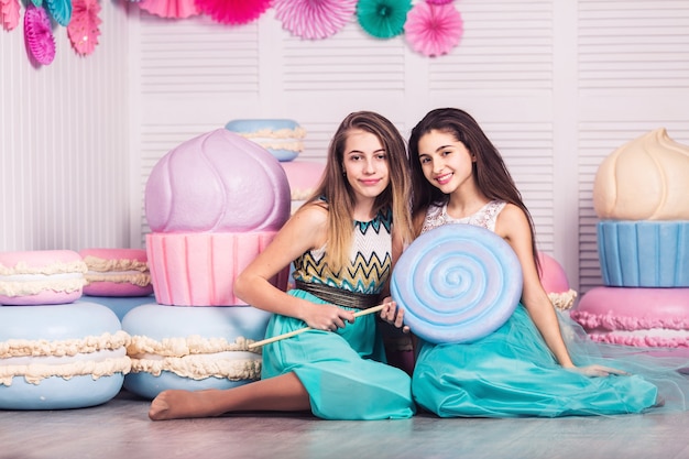 Dos hermosas chicas en vestidos azules sostienen en sus manos enormes dulces y macarrones con decoración de macarrones