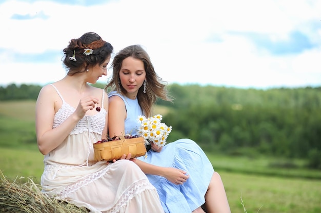 Dos hermosas chicas en vestidos en el campo de verano con bayas