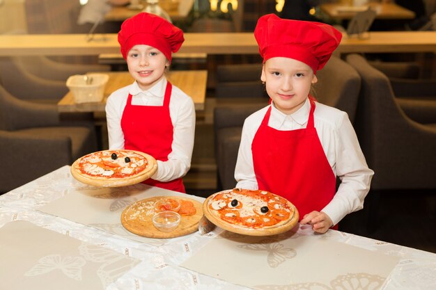 Dos hermosas cocineras con camisas blancas y delantales rojos en el restaurante hacen pizza