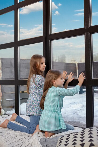 Dos hermosas hermanas caucásicas sentadas en el alféizar de la ventana, vieron algo interesante en la ventana e intentaron verlo.