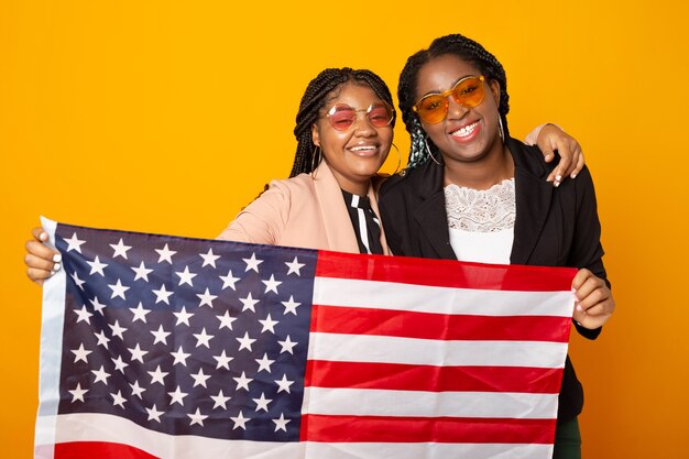 Dos hermosas mujeres africanas con bandera americana sobre fondo amarillo