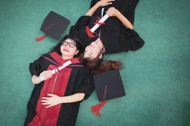 Dos hermosas mujeres asiáticas se encuentran en el césped verde el día de la graduación.