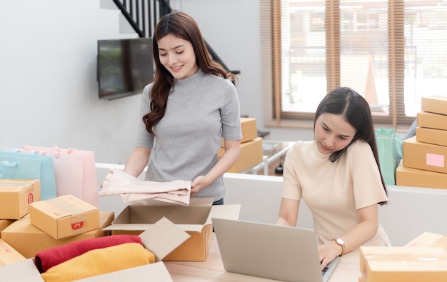 Dos hermosas mujeres asiáticas están comprobando pedidos por computadoras portátiles a través de Internet