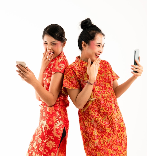 Dos hermosas mujeres en cheongsam rojo de pie juntas miran su teléfono y se ríen